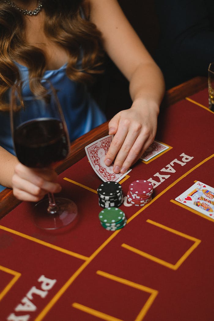 A woman holding cards and a wine glass at a casino, playing poker.